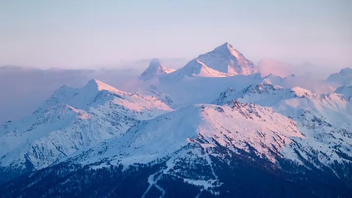A majestic mountain range covered in snow, with a clear blue sky in the background