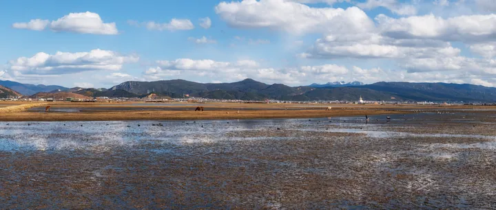 A large body of water surrounded by mountains in the background, with a sky filled with clouds