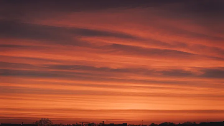 A beautiful sunset over a field with trees in the foreground and clouds in the sky