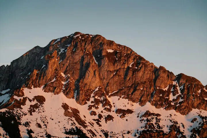A mountain with snow on its peak and a blue sky in the background