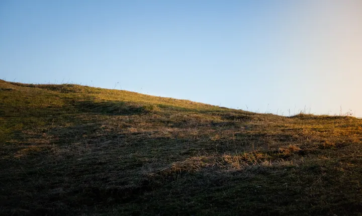 A grassy hill with a blue sky in the background