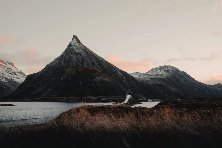 A stunning view of a mountain range with a lake in the foreground, surrounded by lush green grass and snow-capped peaks in the background