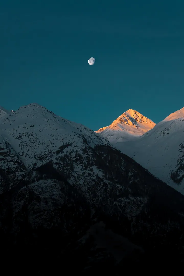 A majestic mountain range with snow-capped peaks illuminated by the light of a full moon in the night sky