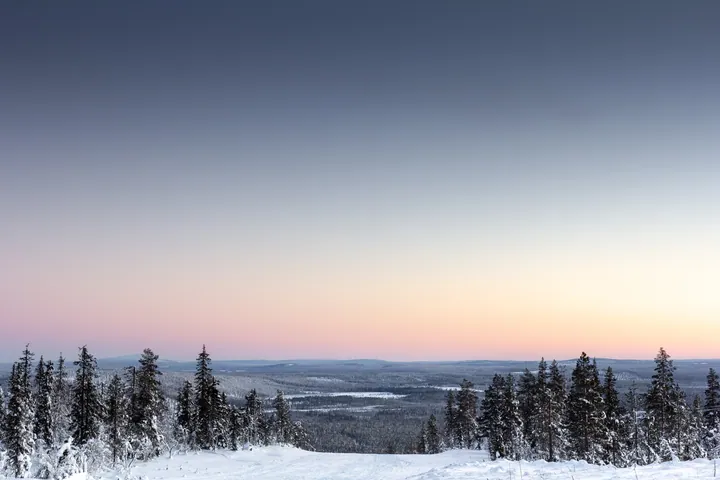 A snow covered field with trees in the foreground and a beautiful sunset in the background