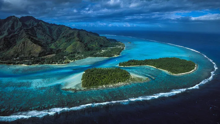 An aerial view of a small island in the middle of the ocean, surrounded by lush green trees and rolling hills