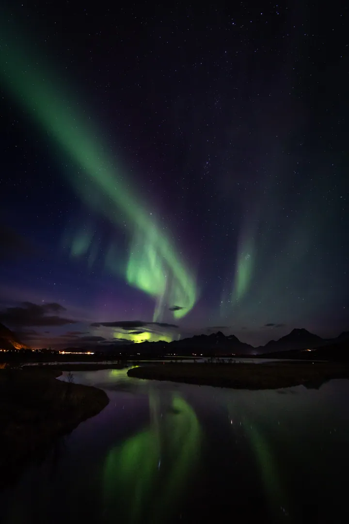 A breathtaking view of the aurora borealis brightly illuminating the night sky over a body of water, with hills and clouds in the background