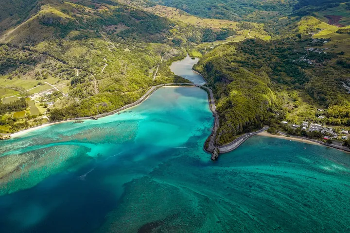 An aerial view of a small island in the middle of a body of water, surrounded by lush green trees and rolling hills