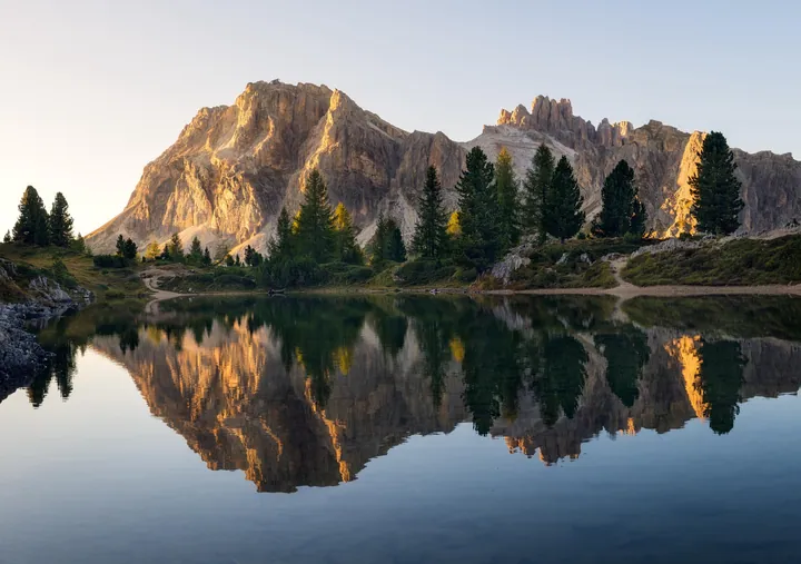 A mountain reflected in a lake at sunset, surrounded by lush green grass, trees, and plants