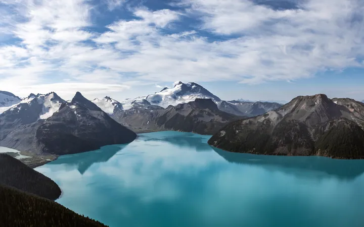 A large body of water surrounded by snow-capped mountains, with a sky filled with clouds in the background