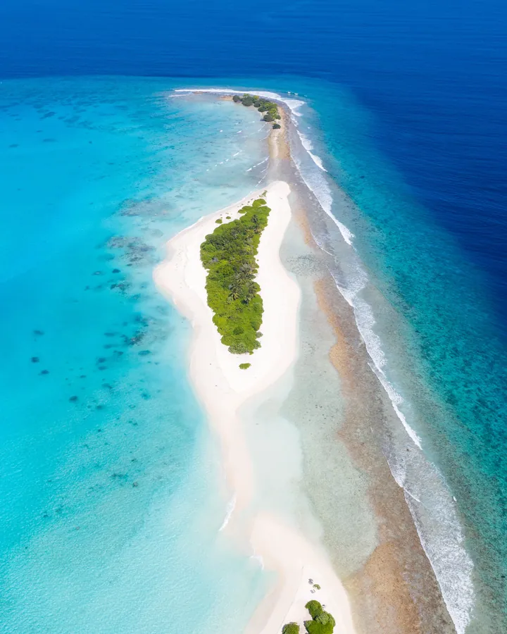 An aerial view of a small island in the middle of the ocean, surrounded by lush green trees and crystal clear blue water