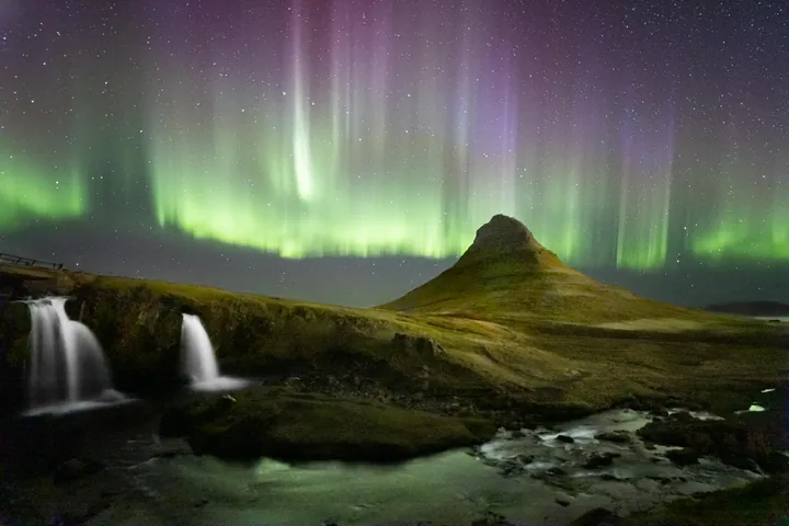 A breathtaking view of the aurora borealis brightly illuminating the night sky above Kirkjufell waterfall in Iceland