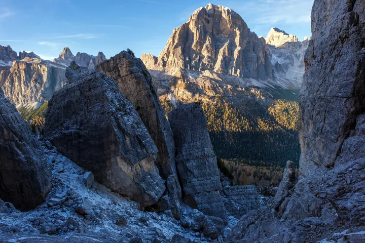 A breathtaking view of the Dolomites in the Italian Alps, with snow-covered mountains, trees, and a sky filled with clouds illuminated by the setting 