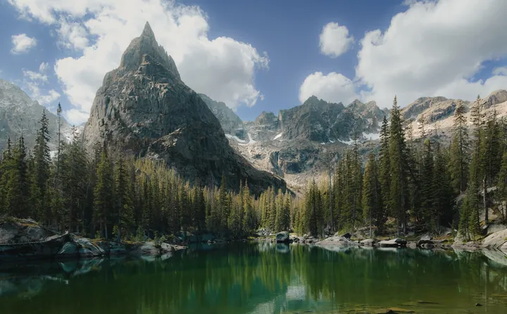 A mountain range with a lake in the foreground, surrounded by trees and rocks