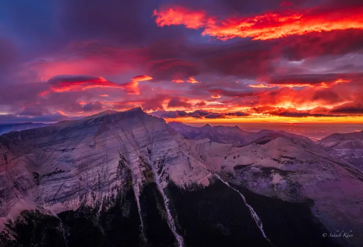 A breathtaking view of a mountain range with a red sky in the background, illuminated by the setting sun