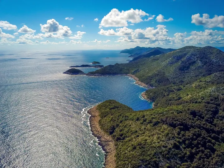 An aerial view of a small island in the middle of the ocean, surrounded by lush green hills and trees