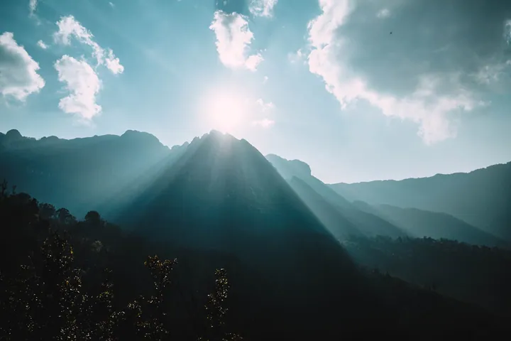 Mountain Range Illuminated By Sunlight Through Clouds wallpapers