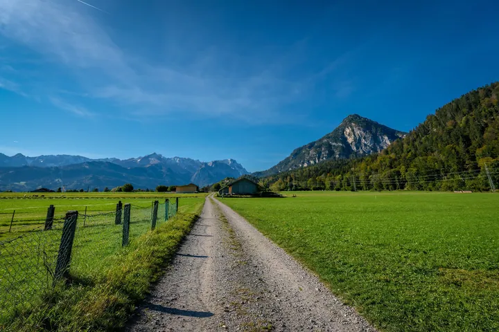 A dirt road winding through a lush green field, with a fence on either side