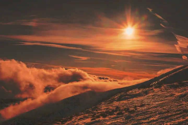 A beautiful sunset over a mountain range with the sun setting in the sky, casting a warm orange glow over the landscape