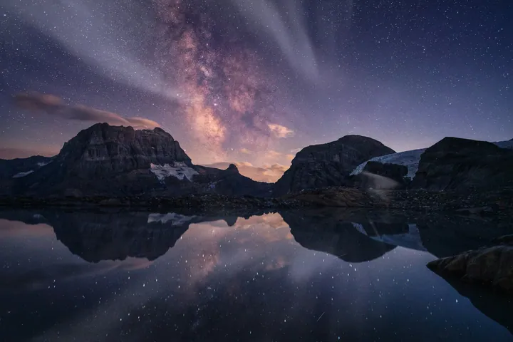 A stunning view of the night sky, with the milky way shining brightly over a mountain range reflected in the still waters below