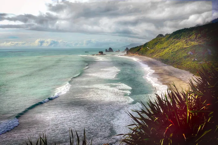 A stunning view of a beach from the top of a hill, with the water lapping against the shoreline, lush green grass and plants swaying in the breeze, an