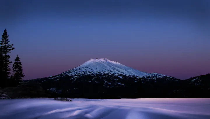 A snow-covered mountain in the middle of a snowy field at night, with trees on the left side and a starry sky in the background
