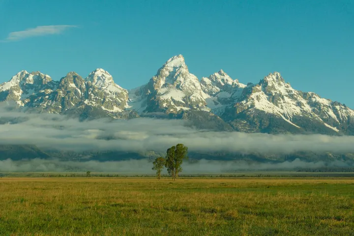Snow-Capped Tetons Amidst Green Plains And Gray Clouds wallpapers