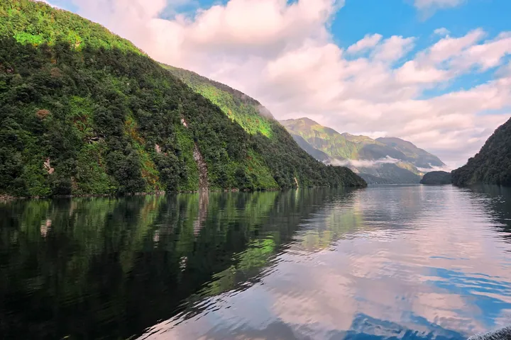 A large body of water surrounded by lush green hills and trees, with a sky full of clouds in the background