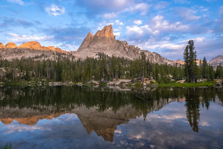 A mountain reflected in a small lake in the middle of a forest, surrounded by trees, rocks, and hills