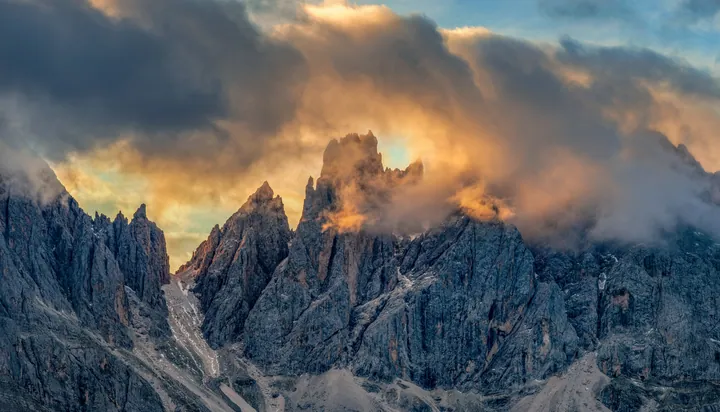 A majestic mountain range with snow-capped peaks and a cloudy sky in the background, illuminated by the setting sun