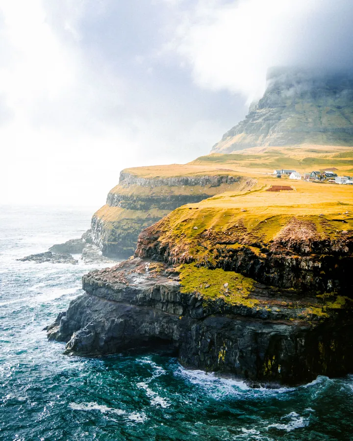 A stunning view of the Faroe Islands, with the water on the left side, hills in the background, and a few houses on the right side