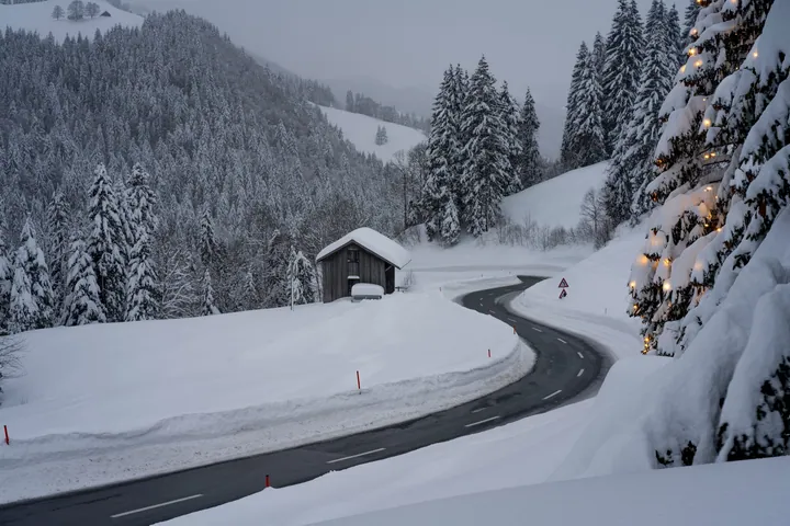 A snowy road winding through a snowy mountain landscape, with a small house in the middle