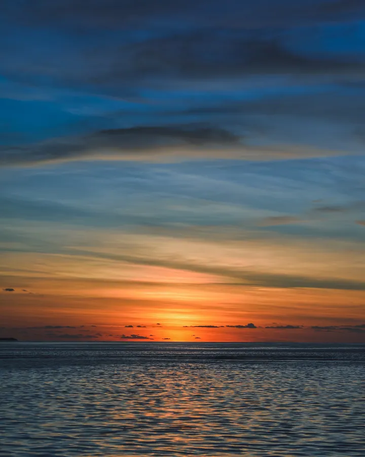 A beautiful sunset over the ocean with the sun setting in the background, casting a warm orange glow over the water and the sky filled with clouds