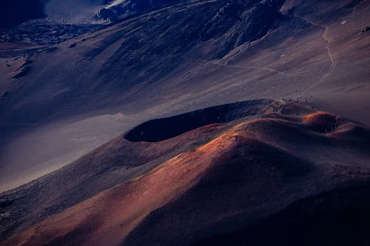 An aerial view of a large crater in the middle of a desert, surrounded by hills and a sky with clouds in the background