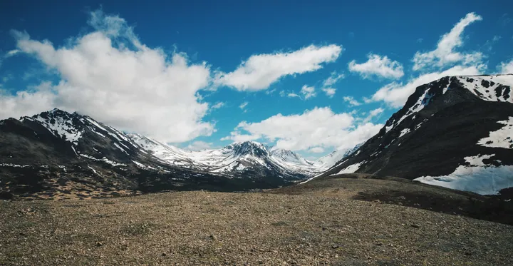Grassy Field With Snow-Capped Mountains And Clouds wallpapers