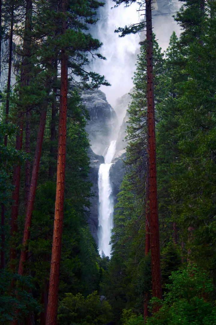 Waterfall Cascading Over Charcoal Rocks Amidst Teal Forest — original wallpaper