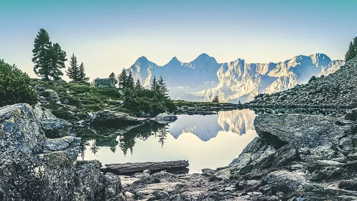 A small lake in the middle of a rocky mountain range, surrounded by trees and hills