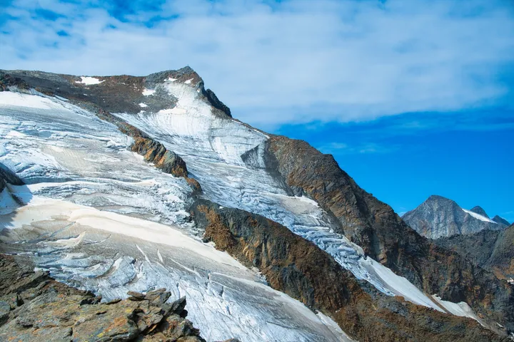 A snow-covered mountain with a glacier in the foreground and a blue sky in the background